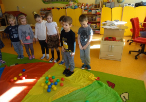 Chłopiec stoi na chuście, na której rozłożone są kolorowe piłki.